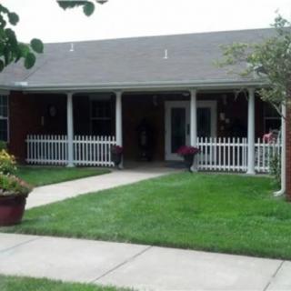 A small house with a front porch and white fence, surrounded by a well-maintained lawn and garden.