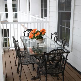 A cozy balcony with a glass table and wrought iron chairs, adorned with a vibrant orange flower centerpiece.