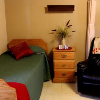 A cozy bedroom with a single bed, nightstand, and a comfortable chair.