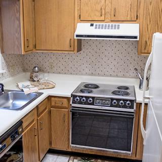 A small kitchen featuring a stove, oven, sink, and refrigerator with wooden cabinets.