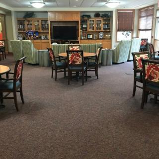 A spacious living room area with multiple tables and chairs, a television, and shelves in the background.