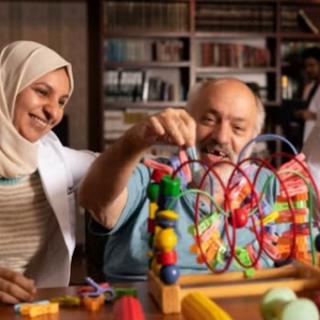 A caregiver engages with an elderly man in interactive play using colorful wooden toys, promoting cognitive and emotional wellness.