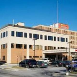 A hospital building with cars parked in front of the entrance.