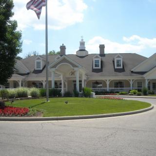 A large, elegant building with a flagpole in the front and well-maintained landscaping under a clear blue sky.