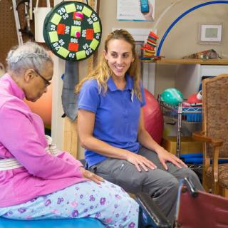 A female therapist assists an elderly woman with physical therapy exercises in a rehabilitation center.