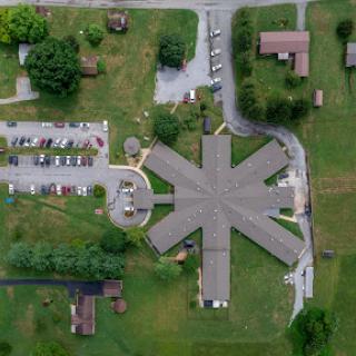 An aerial view of a building complex surrounded by greenery and a parking area.