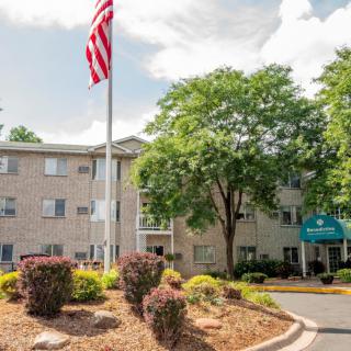 An apartment building with an American flag, surrounded by trees and well-maintained landscaping.