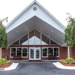 An attractive building entrance with a peaked roof and large windows, surrounded by well-maintained landscaping.