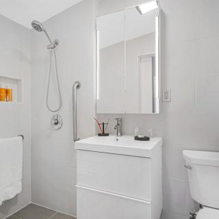 A modern, minimalist bathroom featuring a sleek shower, vanity with mirror, and a toilet.