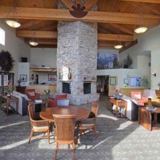 A lobby interior featuring a large stone fireplace, wooden ceiling beams, and seating area with tables and chairs.