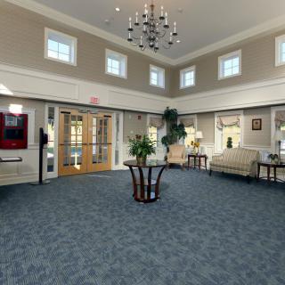 A spacious and elegantly designed lobby with a carpeted floor, chandelier, and comfortable seating.