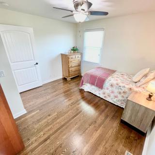A cozy bedroom with a bed, dresser, and nightstand, featuring hardwood floors and a ceiling fan.