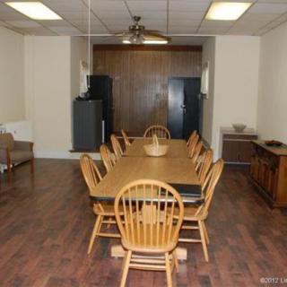 A dining room with a long wooden table, surrounded by chairs and featuring a ceiling fan above.