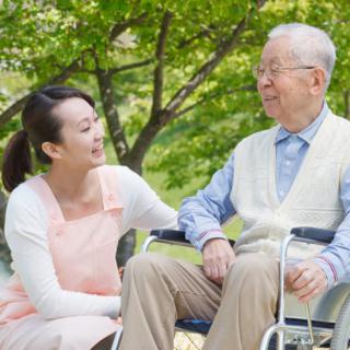 A woman interacts with an elderly man in a wheelchair outdoors.