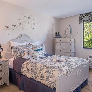 A cozy bedroom with elegant decor, featuring a white and blue color scheme and ample natural light.