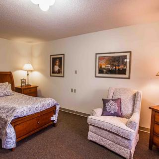 A cozy bedroom with a bed, armchair, and decorative paintings.