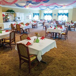 An elegantly decorated dining room with neatly arranged tables and chairs, featuring red table napkins and decorative ceiling drapes.