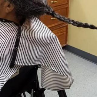 A person in a barbershop chair with a long braided hairstyle.