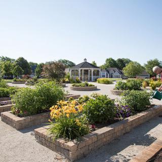 A scenic garden with vibrant flowers and a gazebo in the background on a sunny day.