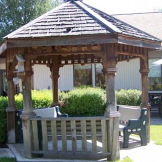 A wooden gazebo with benches set in a garden.