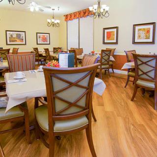 A cozy dining room with neatly arranged tables and chairs, featuring artwork on the walls and warm wood flooring.