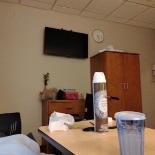 A view of a hospital room with a television, clock, and some items on the table.