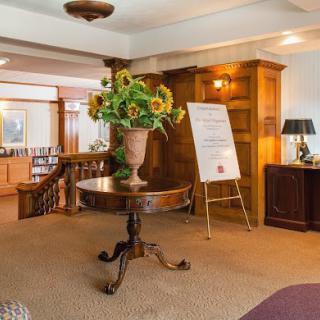 A welcoming hotel lobby with a central table adorned with a vase of sunflowers and wood paneling accents.