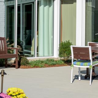 A patio area with outdoor furniture, including chairs and a bench, surrounded by plants and flowers.