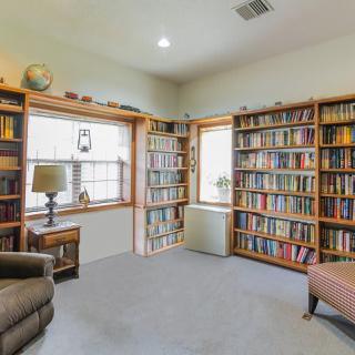 A cozy reading room with bookshelves filled with books, an armchair, and natural light from the windows.