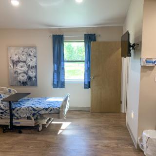 A cozy hospital room featuring a bed, window with blue curtains, and a wall-mounted TV.