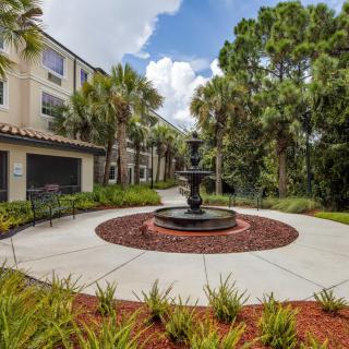 A scenic view of an apartment complex courtyard featuring a central fountain surrounded by palm trees and well-maintained landscaping.