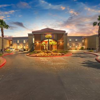 A welcoming hotel entrance at dusk, surrounded by palm trees and illuminated with warm lights.