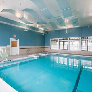 A well-lit indoor swimming pool with blue walls and large windows.