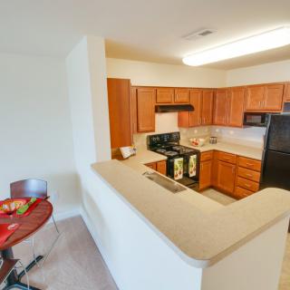 A modern apartment kitchen with wooden cabinets and a small dining area.