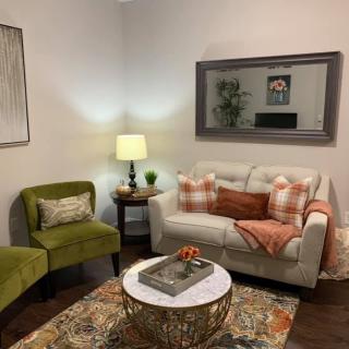 A cozy living room with a white sofa adorned with pillows, a green armchair, and a decorative coffee table, illuminated by a warm lamp.