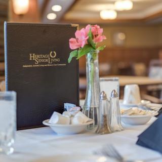 A well-set restaurant table with a menu and flowers.