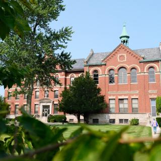 A historic brick building surrounded by trees and greenery.