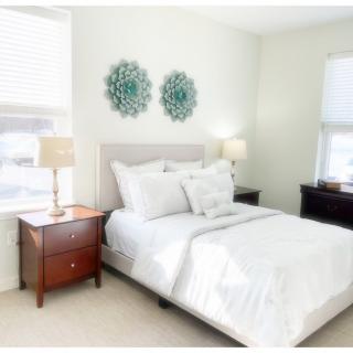 A bright and cozy bedroom with elegant decor, featuring a neatly made bed, bedside tables, lamps, and wall art.