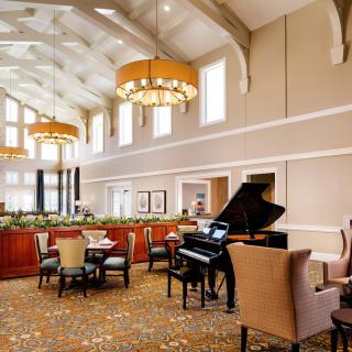 A spacious lounge with comfortable seating, featuring a grand piano and elegant chandeliers.