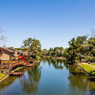 A serene residential area with houses along a calm river, surrounded by lush trees.