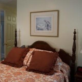 A cozy bedroom with a wooden bed and framed artwork above.