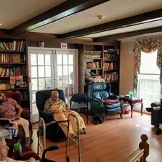 A cozy living room with seniors relaxing, surrounded by bookshelves and comfortable seating.