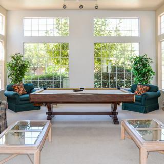 A bright living room featuring a shuffleboard table, large windows, and comfortable seating.