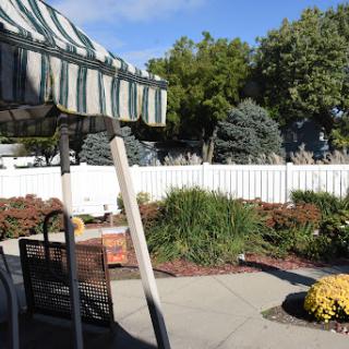 A serene outdoor garden space featuring colorful flowers and green trees, complemented by a striped awning.