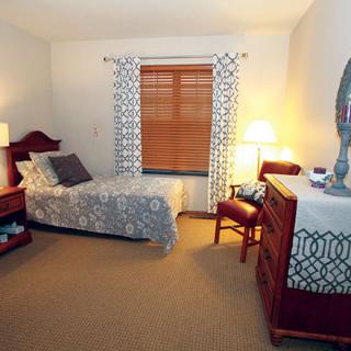 A cozy bedroom with a single bed, dresser, and warm lighting.