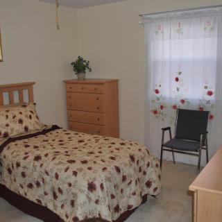A cozy bedroom with a single bed, dresser, and chair by the window.