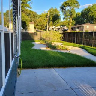 A sunny backyard with a patio, grassy area, and surrounding trees.