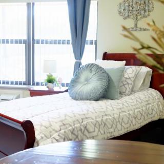 A cozy bedroom with a neatly made bed, decorative pillows, and large windows with curtains.