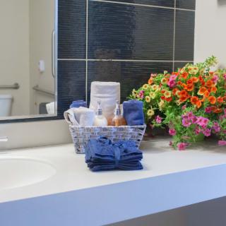 A tidy bathroom counter with neatly arranged towels, toiletries in a basket, and colorful flowers.