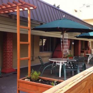 A cozy outdoor patio area with tables, chairs, umbrellas, and wooden planters under a pergola.
